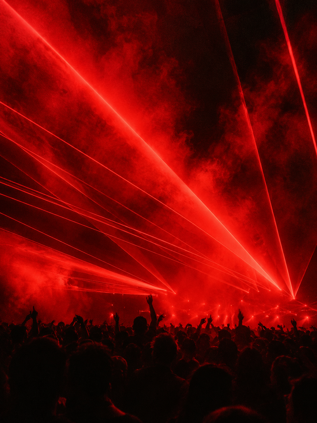 Red lasers cutting through haze above a rave crowd